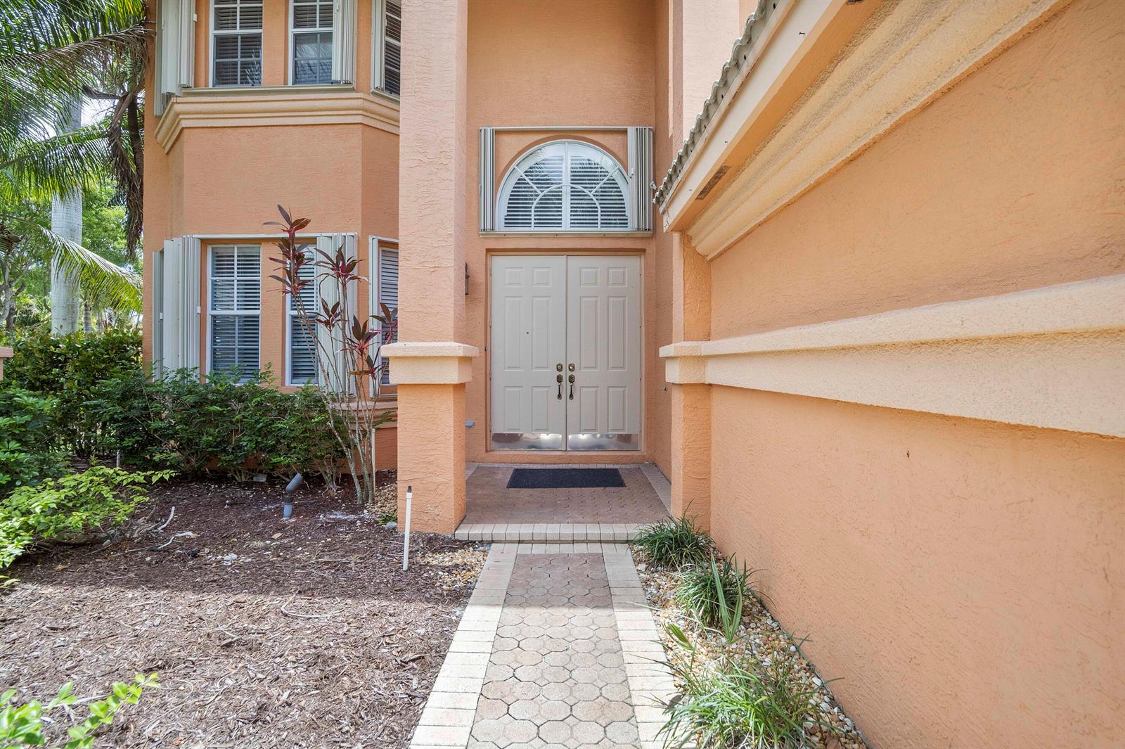 The exterior of a peach-colored house features a double front door and a paved walkway — 6370 Stonehurst Circle, Lake Worth FL 33467, LAKE WORTH, FL