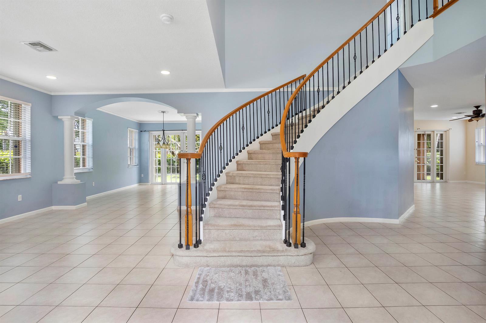 A curved staircase with carpeted steps and a wooden handrail sits in a tiled foyer — 6370 Stonehurst Circle, Lake Worth FL 33467, LAKE WORTH, FL