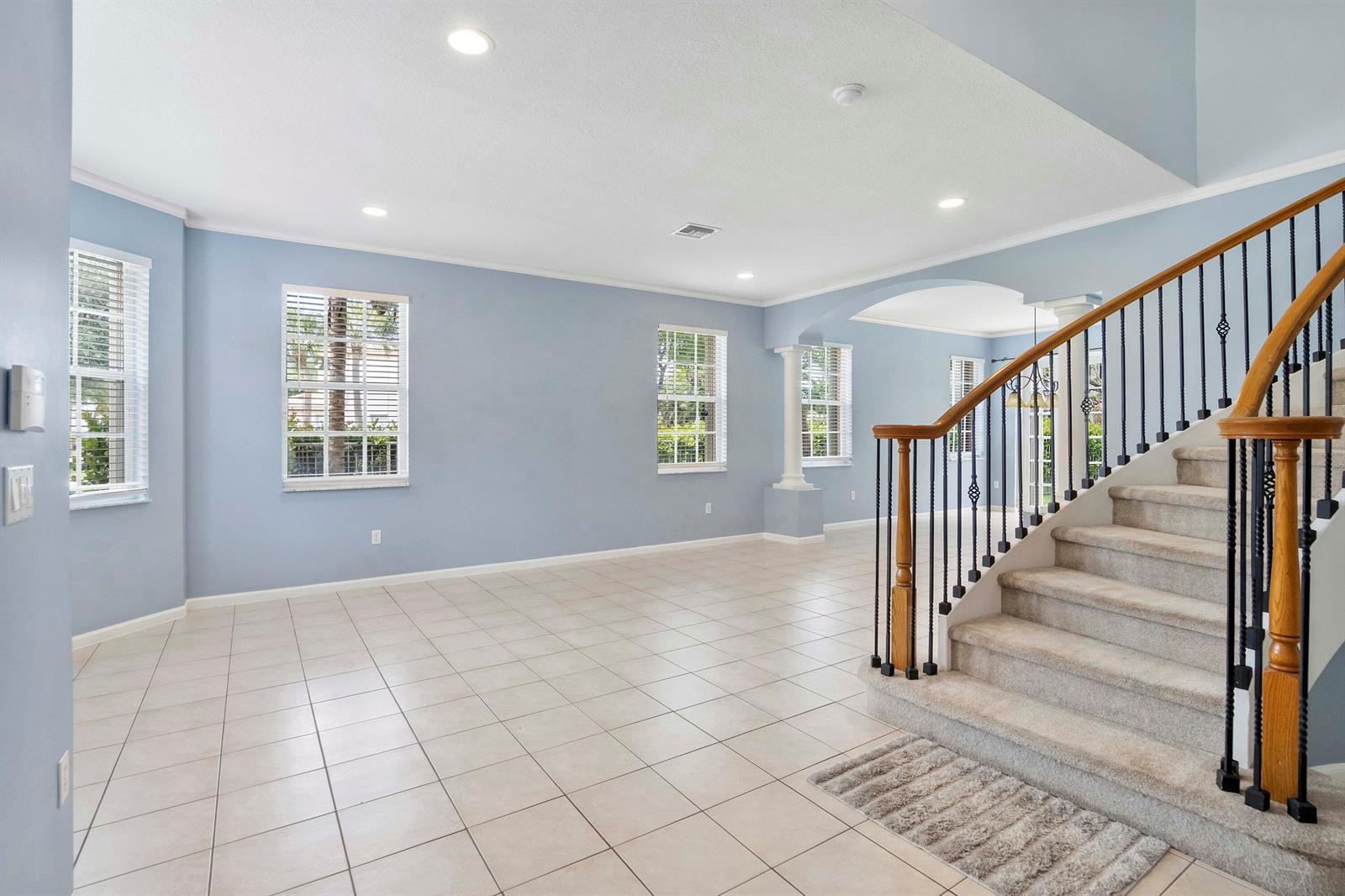 An empty room with light blue walls, tile flooring, and a carpeted staircase with railings — 6370 Stonehurst Circle, Lake Worth FL 33467, LAKE WORTH, FL