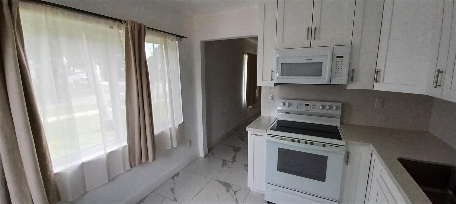 A kitchen features white cabinetry, a white stove, a microwave, and light-colored tile flooring — 602 SE 2nd Avenue, Dania Beach FL 33004, DANIA BEACH, FL
