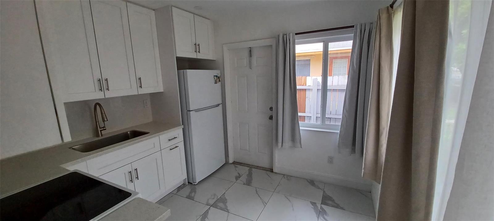 A small kitchen features white cabinets, a white refrigerator, a sink, and light-colored tile flooring — 602 SE 2nd Avenue, Dania Beach FL 33004, DANIA BEACH, FL