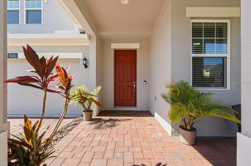 A red front door is centered under a covered entryway with brick pavers and plants — 5026 DOWN COURT, ST CLOUD, FL