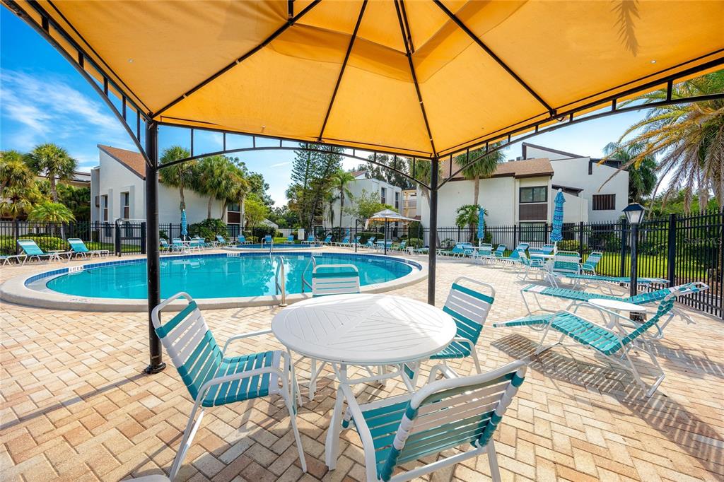 A swimming pool area features a yellow gazebo, patio furniture, and surrounding apartment buildings — 2207 BELLEAIR ROAD UNIT B30, CLEARWATER, FL