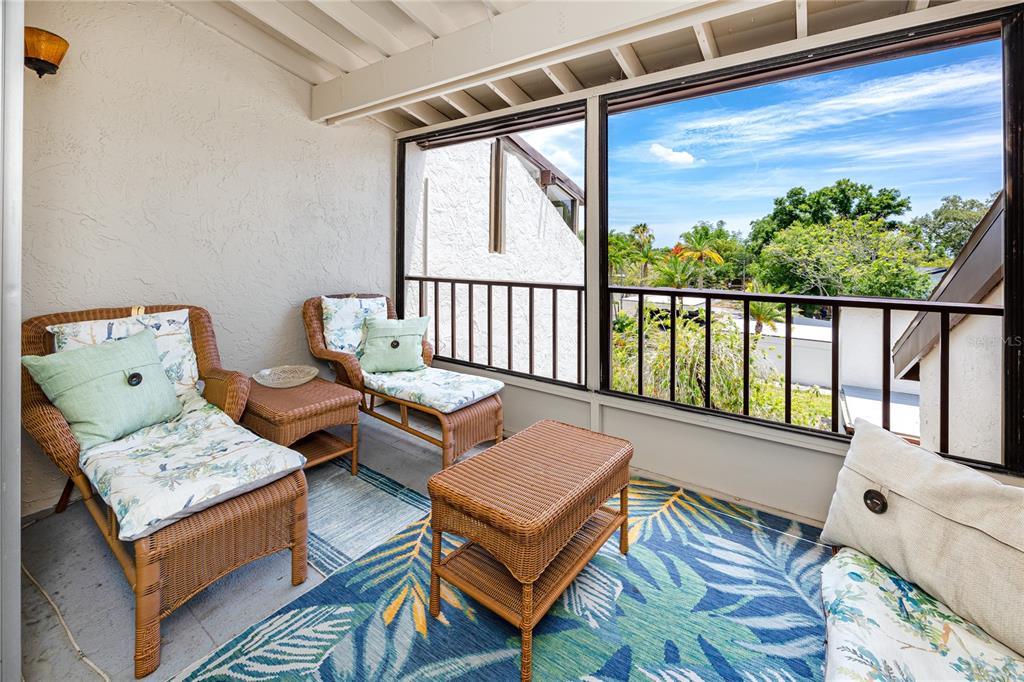 A screened-in balcony features wicker furniture, a tropical-patterned rug, and views of trees and sky — 2207 BELLEAIR ROAD UNIT B30, CLEARWATER, FL