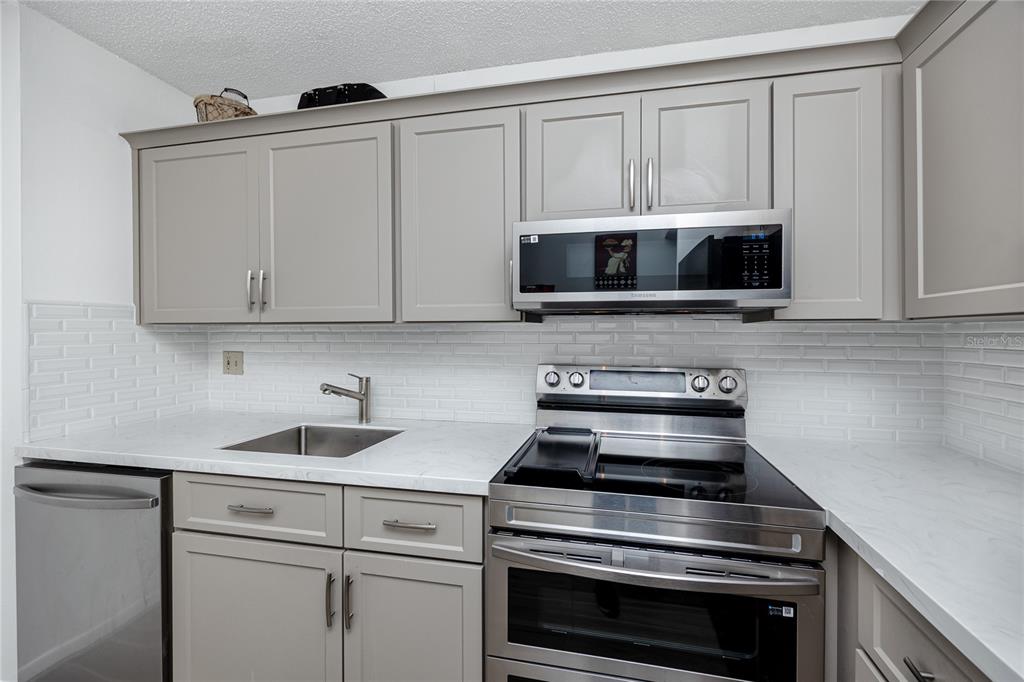A kitchen features gray cabinets, stainless steel appliances, a white backsplash, and marble-look countertops — 2207 BELLEAIR ROAD UNIT B30, CLEARWATER, FL