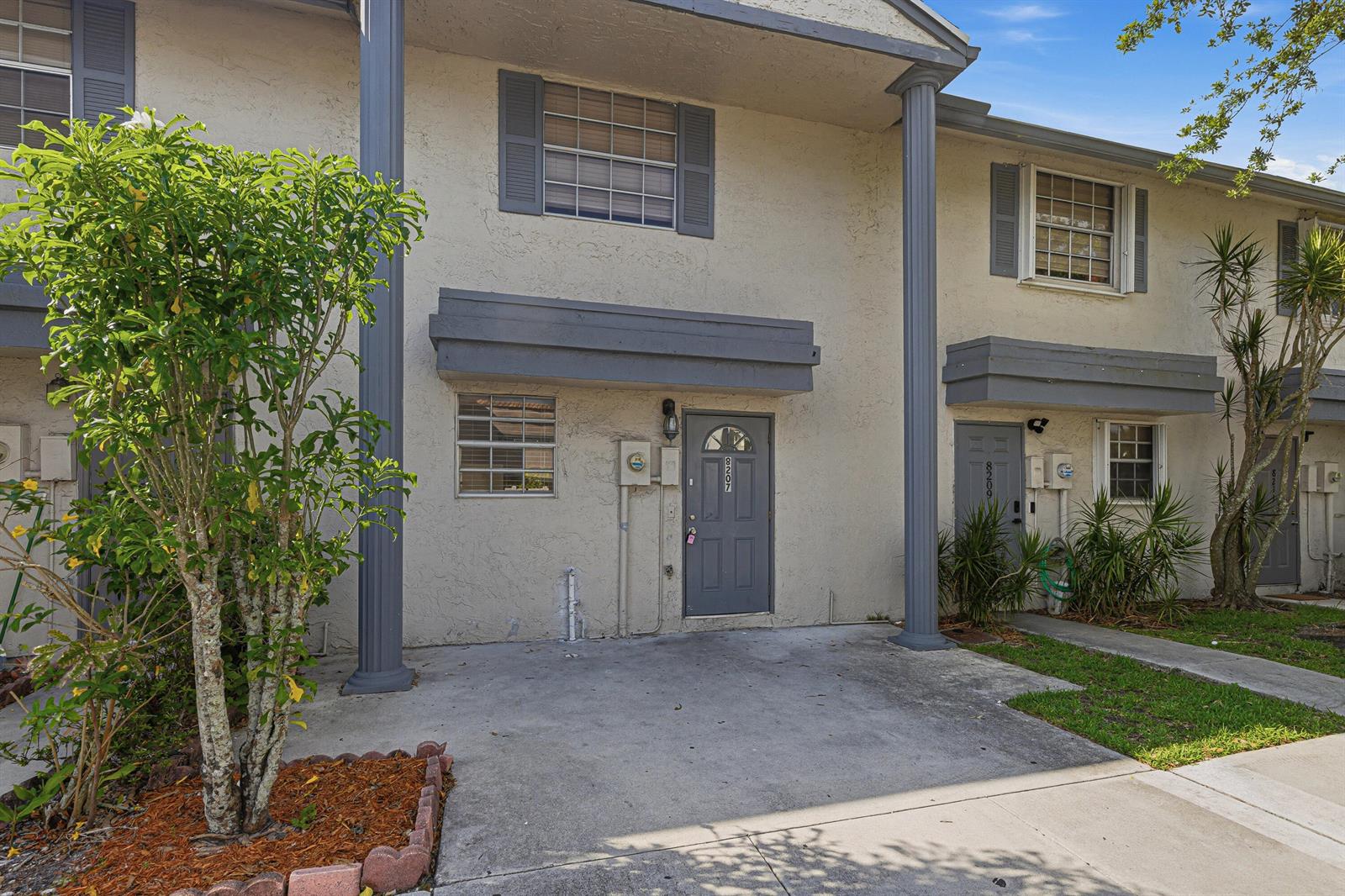 A two-story townhouse exterior features a concrete driveway, gray doors, and decorative columns — 8207 Fairway Road # 8207, Sunrise FL 33351, SUNRISE, FL