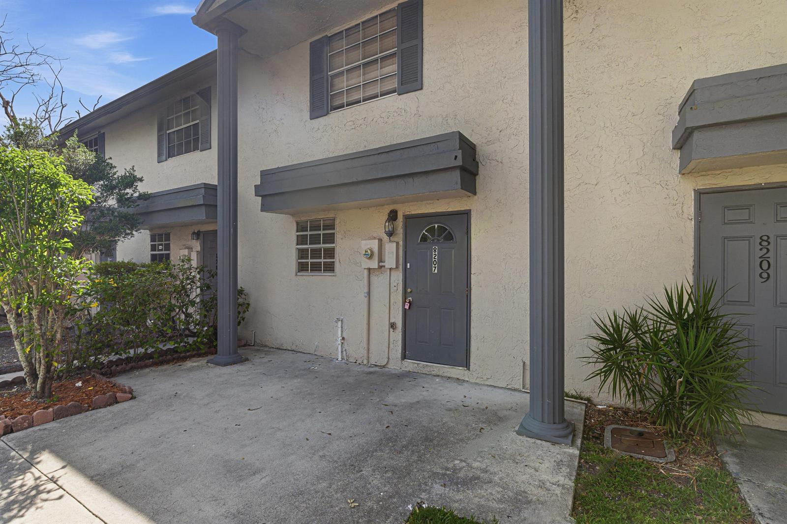 The exterior of a two-story townhouse features a concrete patio, gray doors, and columns — 8207 Fairway Road # 8207, Sunrise FL 33351, SUNRISE, FL
