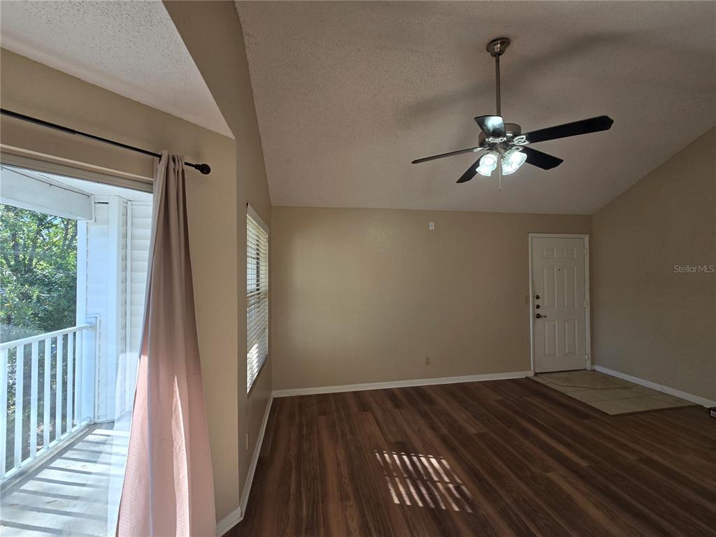 An empty living room features wood-look flooring, a vaulted ceiling, a ceiling fan, and balcony access — 11582 WESTWOOD BOULEVARD UNIT 1436, ORLANDO, FL