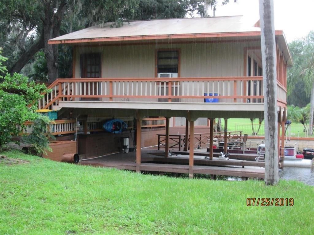 An elevated wooden house with a deck and boat slip sits above a grassy yard — 2690 E LAKE ROAD, KISSIMMEE, FL