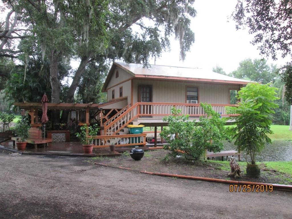 An elevated wooden house with a deck, stairs, and a pergola sits near a pond — 2690 E LAKE ROAD, KISSIMMEE, FL