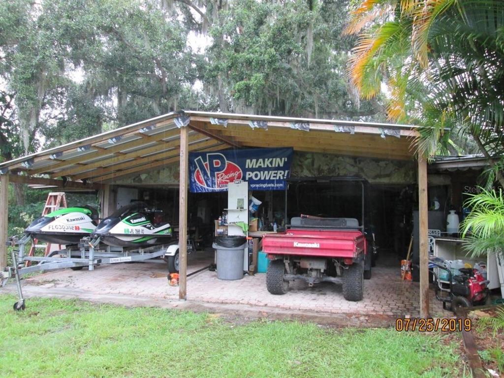 A covered outdoor storage area with two jet skis on trailers and a utility vehicle — 2690 E LAKE ROAD, KISSIMMEE, FL