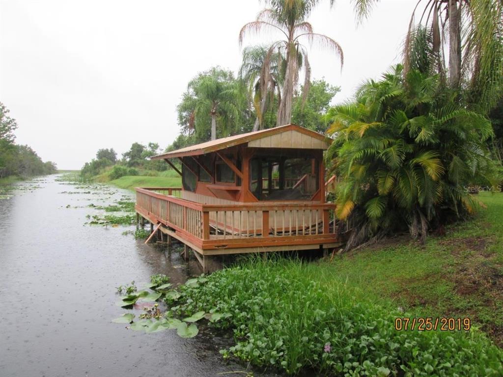 A wooden deck with a screened-in structure sits over a canal next to palm trees — 2690 E LAKE ROAD, KISSIMMEE, FL