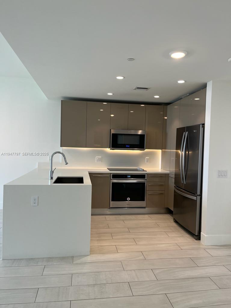 A modern kitchen features taupe flat-panel cabinets, stainless steel appliances, and white quartz countertops — 2000 Metropica Way # 1602, Sunrise FL 33323, SUNRISE, FL