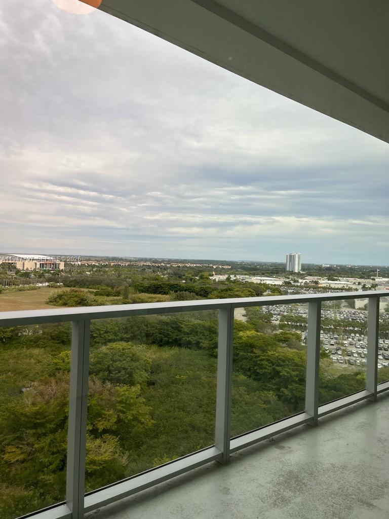 A view from a high-rise balcony overlooking a green landscape and a distant parking lot — 2000 Metropica Way # 1602, Sunrise FL 33323, SUNRISE, FL