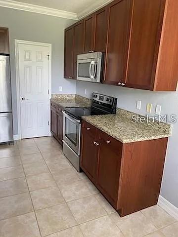 A kitchen features wood cabinets, granite countertops, stainless steel appliances, and light-colored tile flooring — 4511 BAY SPRING COURT, TAMPA, FL