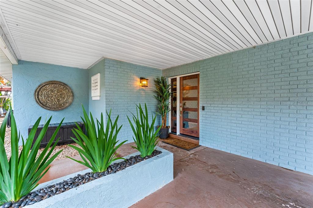 A covered front porch features a blue brick exterior, a wooden door, and a planter — 29 PELICAN LANE, EDGEWATER, FL