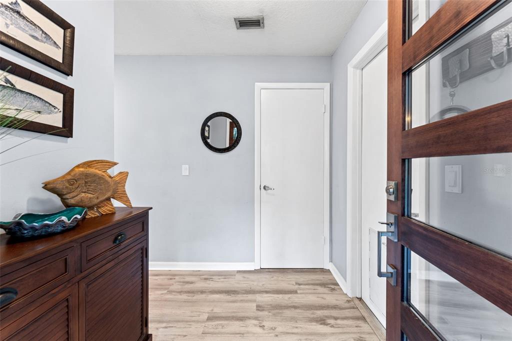 An entryway features wood-look flooring, a dark wood cabinet, and a glass-paneled front door — 29 PELICAN LANE, EDGEWATER, FL
