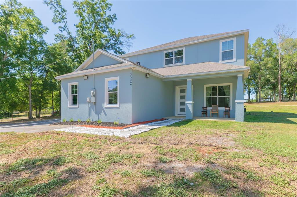 A two-story light blue house with a covered front porch and a white stone walkway — 35369 RUFFING ROAD, DADE CITY, FL