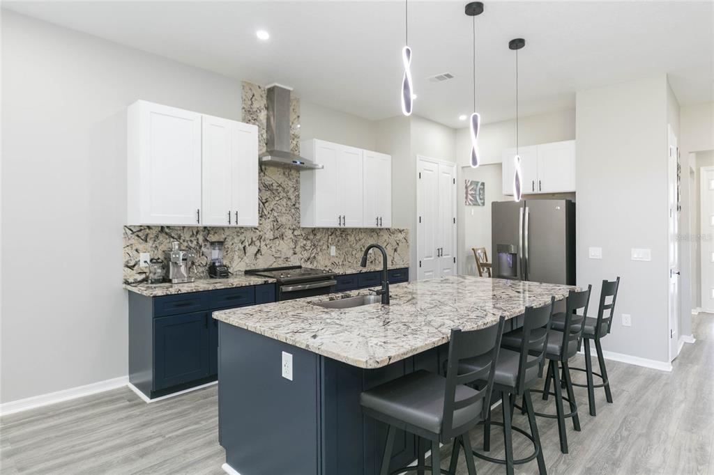 A modern kitchen features dark blue lower cabinets, white upper cabinets, and a granite island — 35369 RUFFING ROAD, DADE CITY, FL