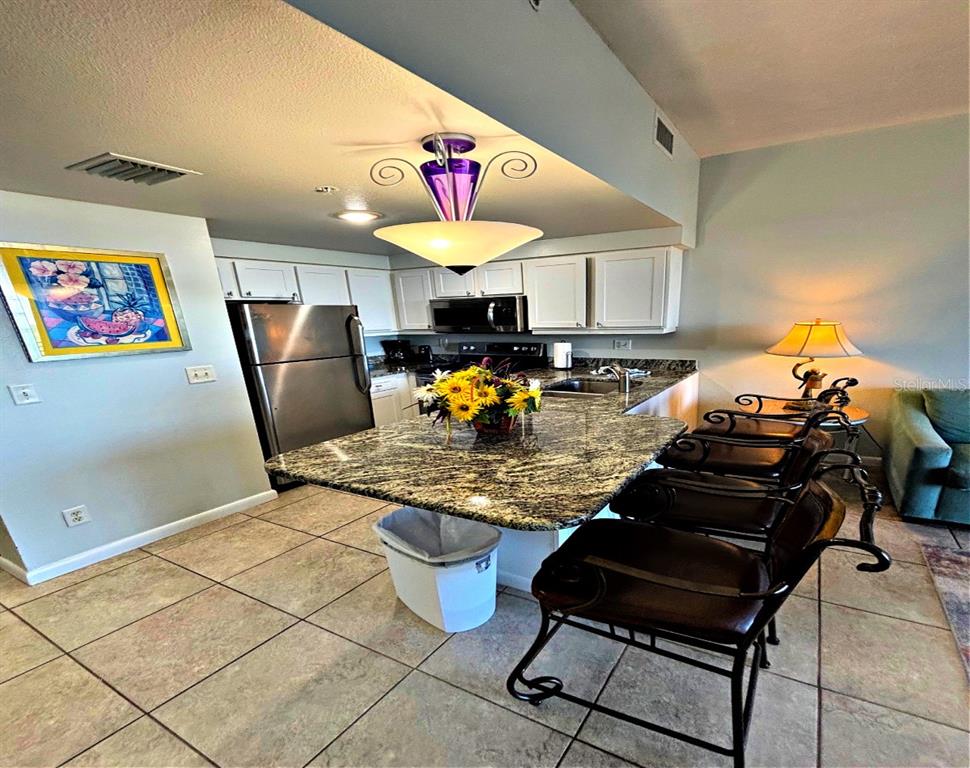 A kitchen features a granite-topped island, stainless steel appliances, white cabinets, and tile flooring — 300 N ATLANTIC AVENUE UNIT 1908, DAYTONA BEACH, FL