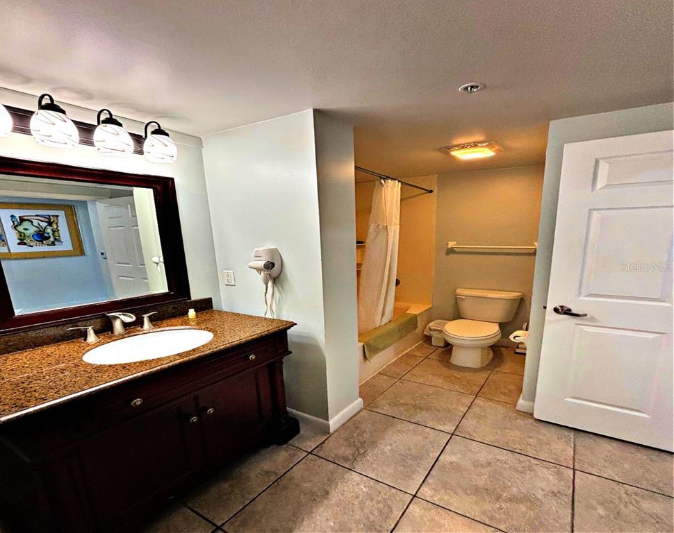 A bathroom features a dark wood vanity with a granite countertop, tile flooring, and a shower — 300 N ATLANTIC AVENUE UNIT 1908, DAYTONA BEACH, FL