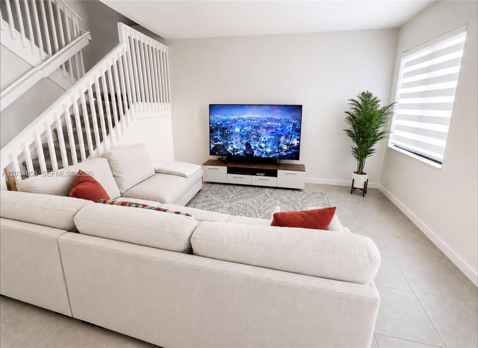 A living room features a white sectional sofa, a television on a stand, and stairs — 20866 NE 7th Pl, Miami FL 33179, MIAMI, FL