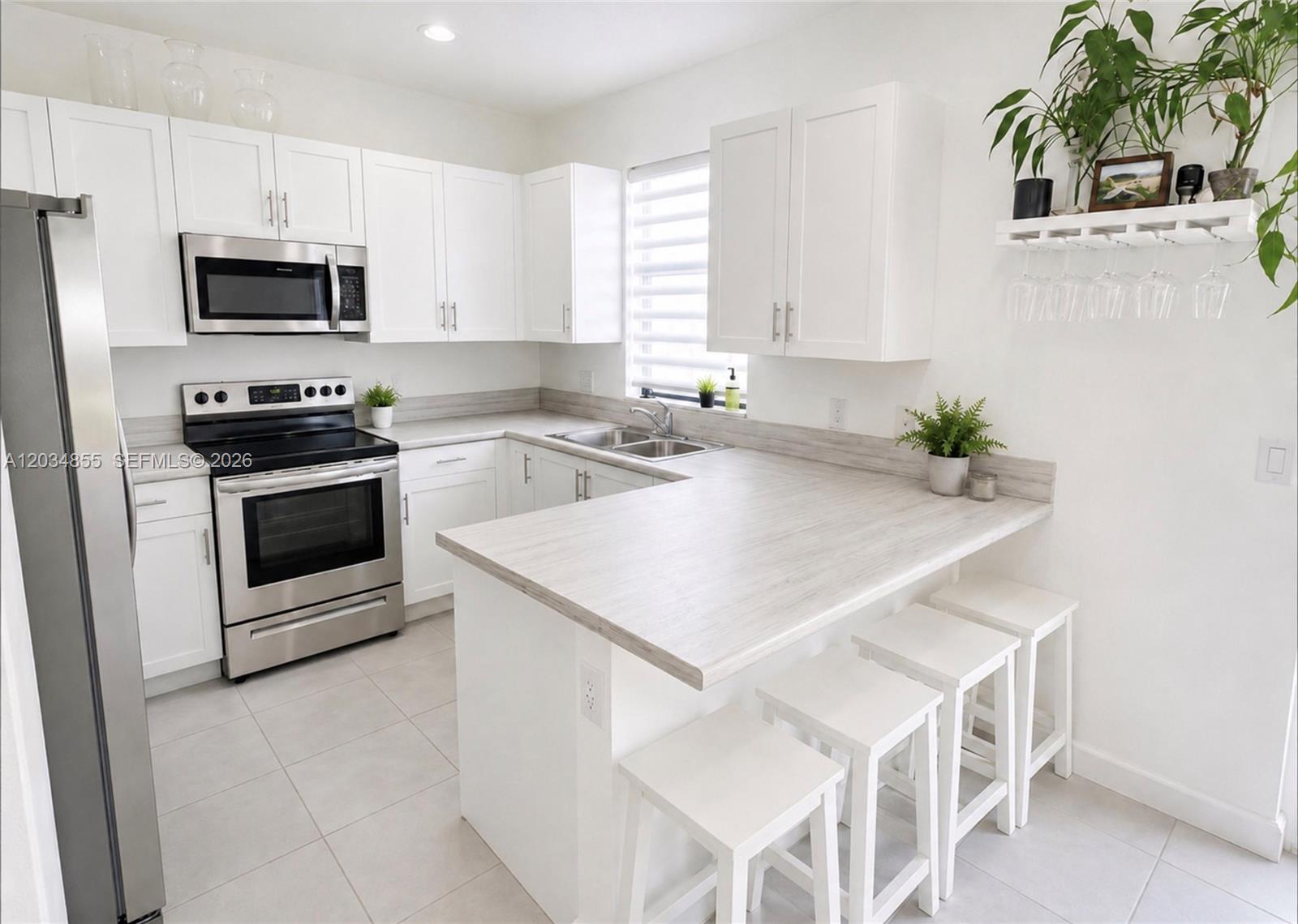 A modern kitchen features white cabinets, stainless steel appliances, and a light wood-grain countertop — 20866 NE 7th Pl, Miami FL 33179, MIAMI, FL