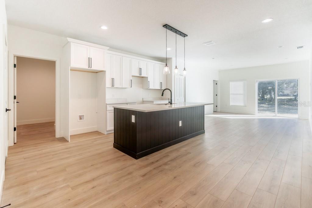 A kitchen with white cabinets, a dark island, and light wood flooring in an open space — 50 W 12TH STREET, APOPKA, FL
