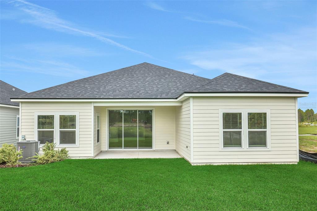 The rear exterior of a single-story house features light siding, a sliding glass door, and windows — 47 WINDMILL PALM WAY, PALM COAST, FL