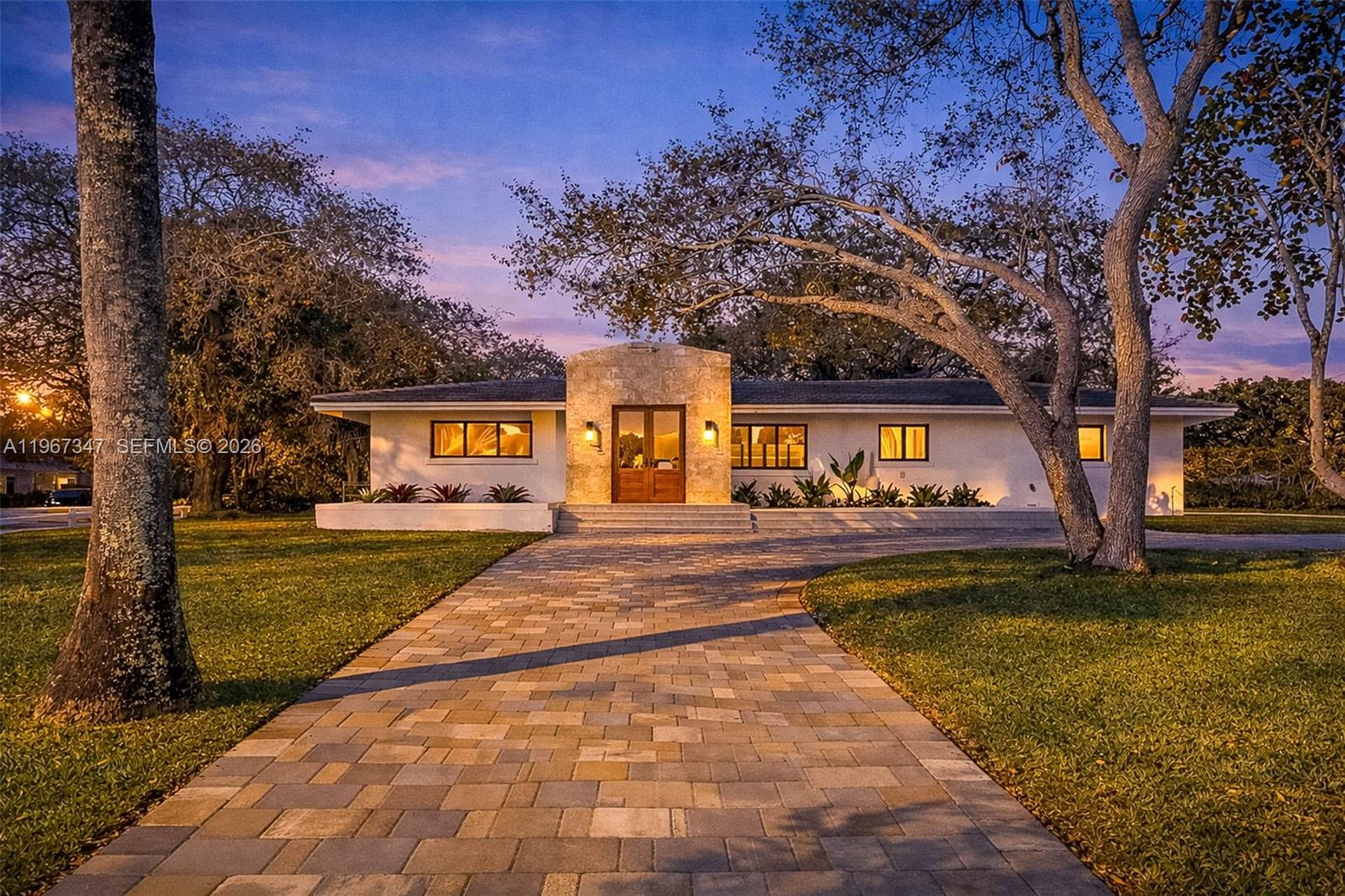 A single-story house with a stone entryway and a paved driveway at twilight — 12940 SW 73rd Ave, Pinecrest FL 33156, PINECREST, FL