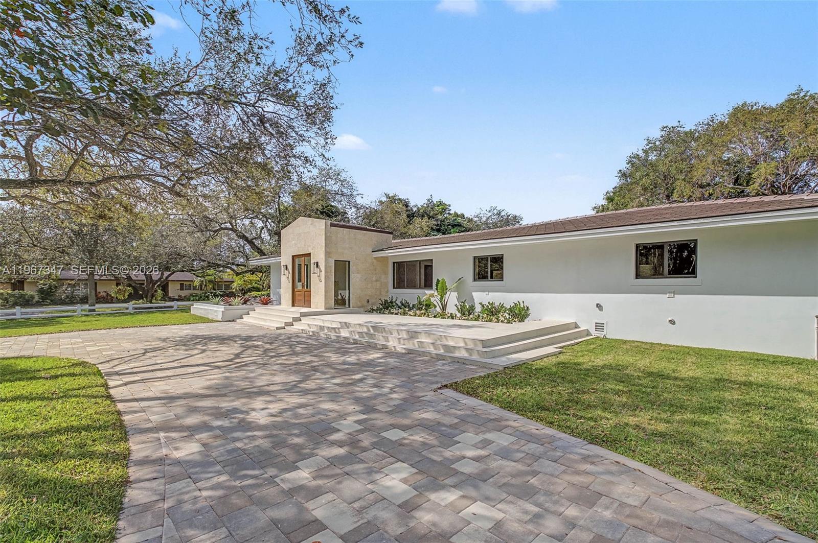 A single-story house with a white exterior, stone entryway, and a large paver driveway — 12940 SW 73rd Ave, Pinecrest FL 33156, PINECREST, FL