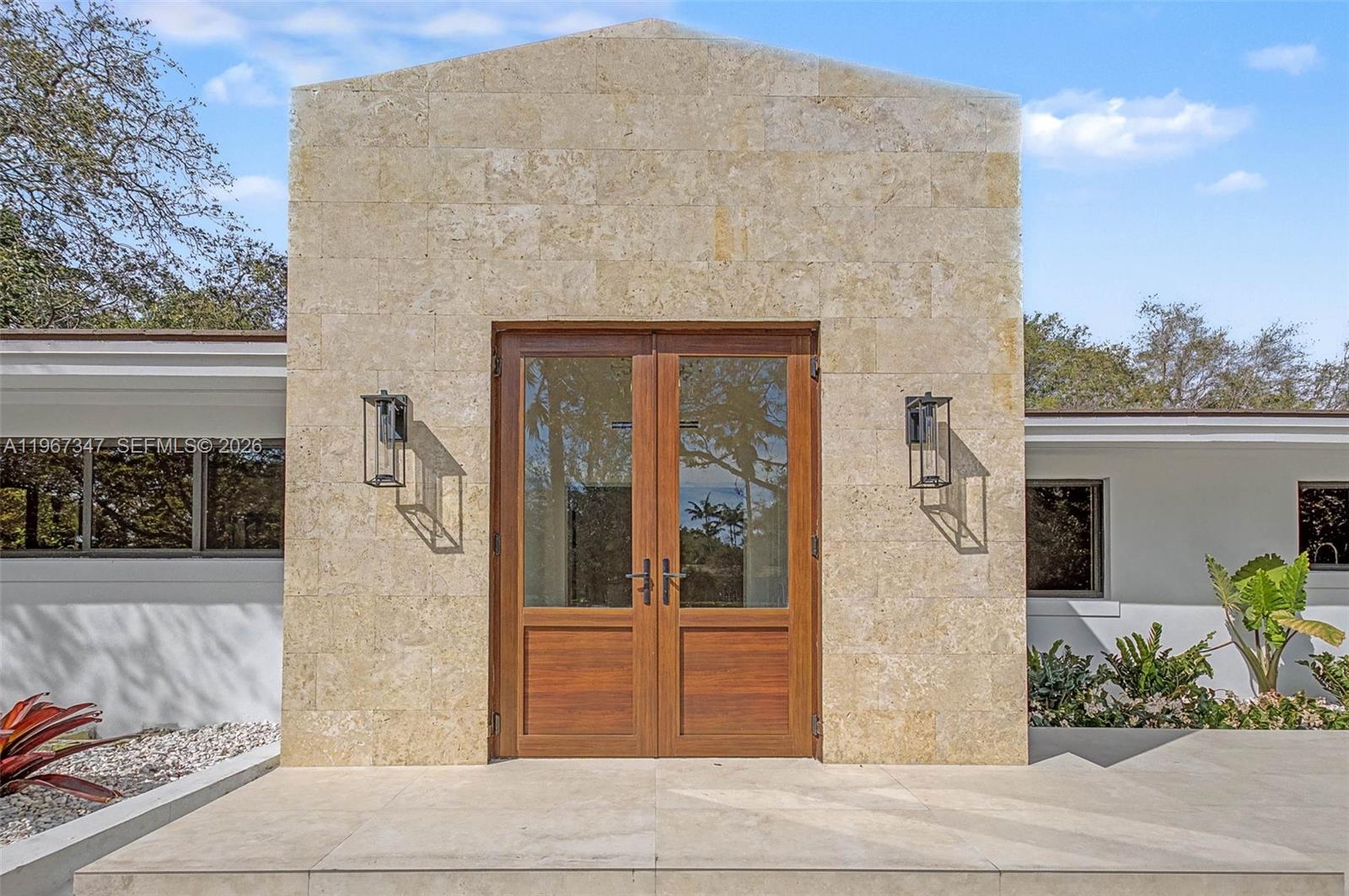 A stone-clad entryway features double wooden doors flanked by two black wall-mounted lanterns — 12940 SW 73rd Ave, Pinecrest FL 33156, PINECREST, FL