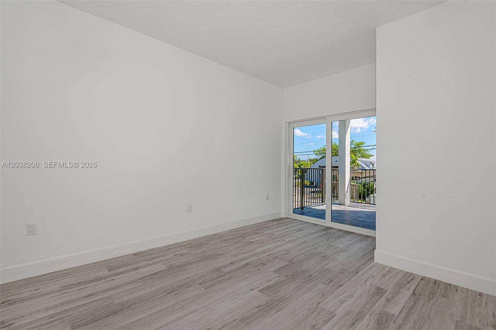 An empty room features light wood-look flooring, white walls, and a sliding glass door to a balcony — 635 NW 30 terrace, Pompano Beach FL 33069, POMPANO BEACH, FL