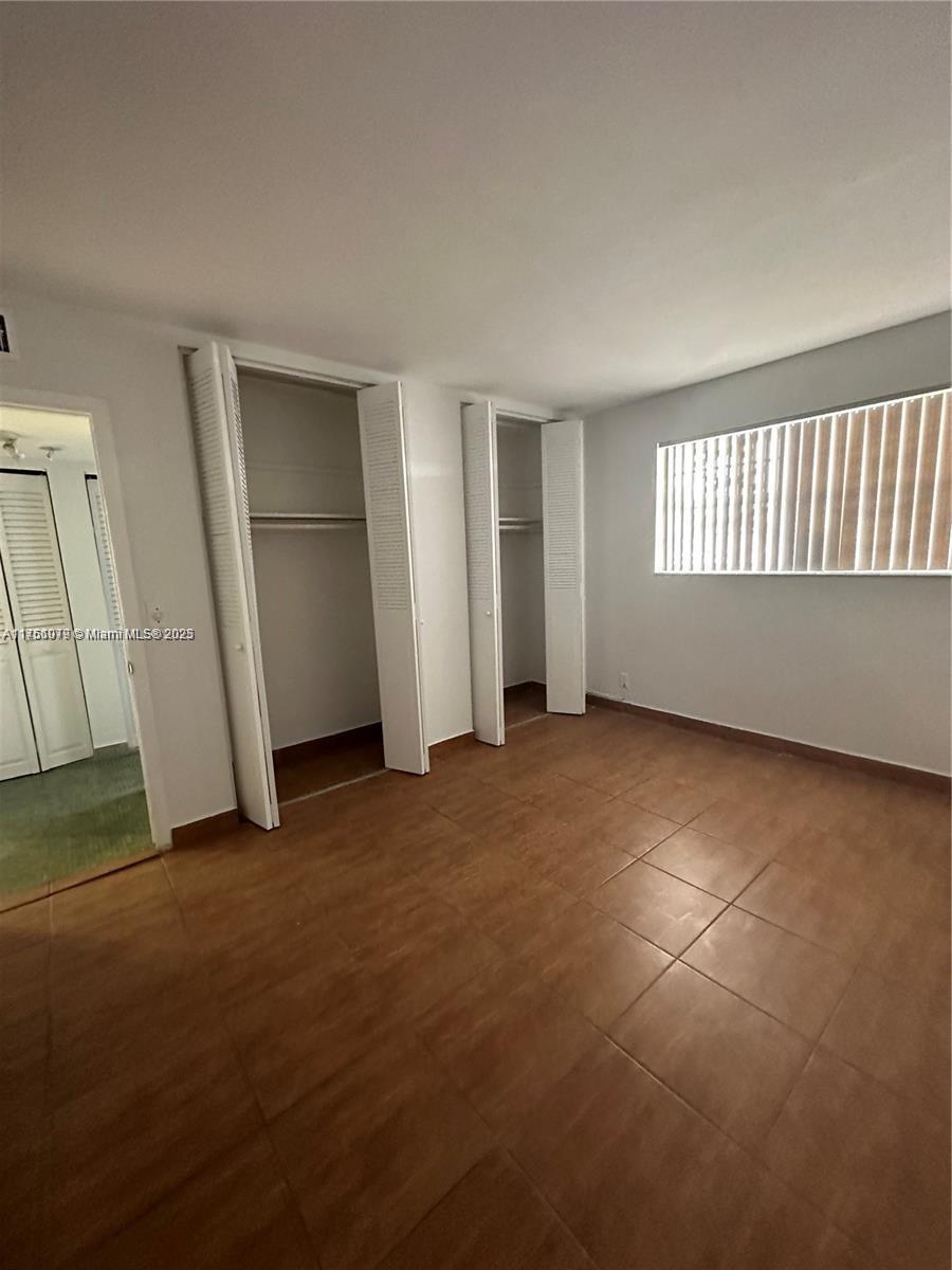 An empty bedroom features light-colored walls, tiled flooring, and two sets of louvered closet doors — 1100 NE 1st Ct # 105, Hallandale Beach FL 33009, HALLANDALE BEACH, FL