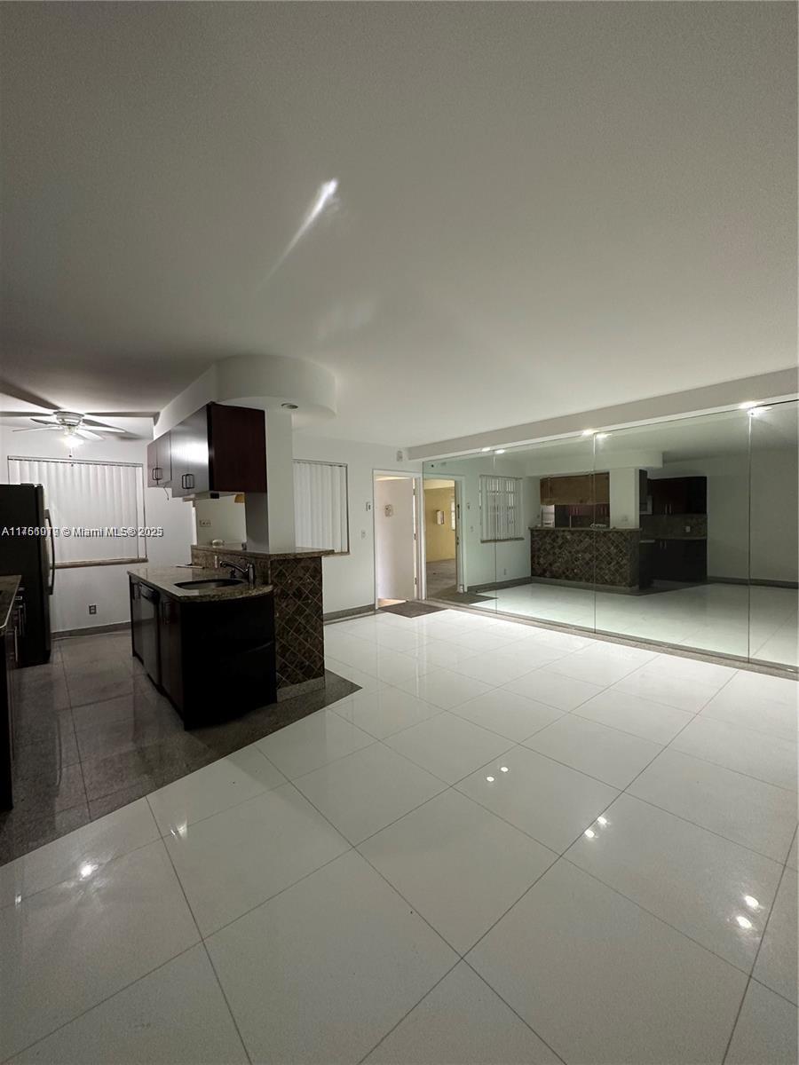 A kitchen with dark cabinets and a breakfast bar overlooks a tiled living area — 1100 NE 1st Ct # 105, Hallandale Beach FL 33009, HALLANDALE BEACH, FL