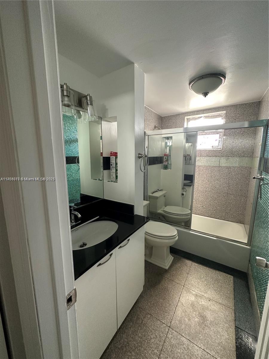 A bathroom features a white vanity with a black countertop, a toilet, and a shower-tub — 1100 NE 1st Ct # 105, Hallandale Beach FL 33009, HALLANDALE BEACH, FL