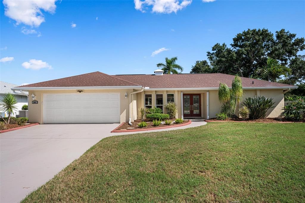 A single-story house with a beige exterior, a two-car garage, and a brown shingled roof — 1011 PINE FOREST COURT, VENICE, FL
