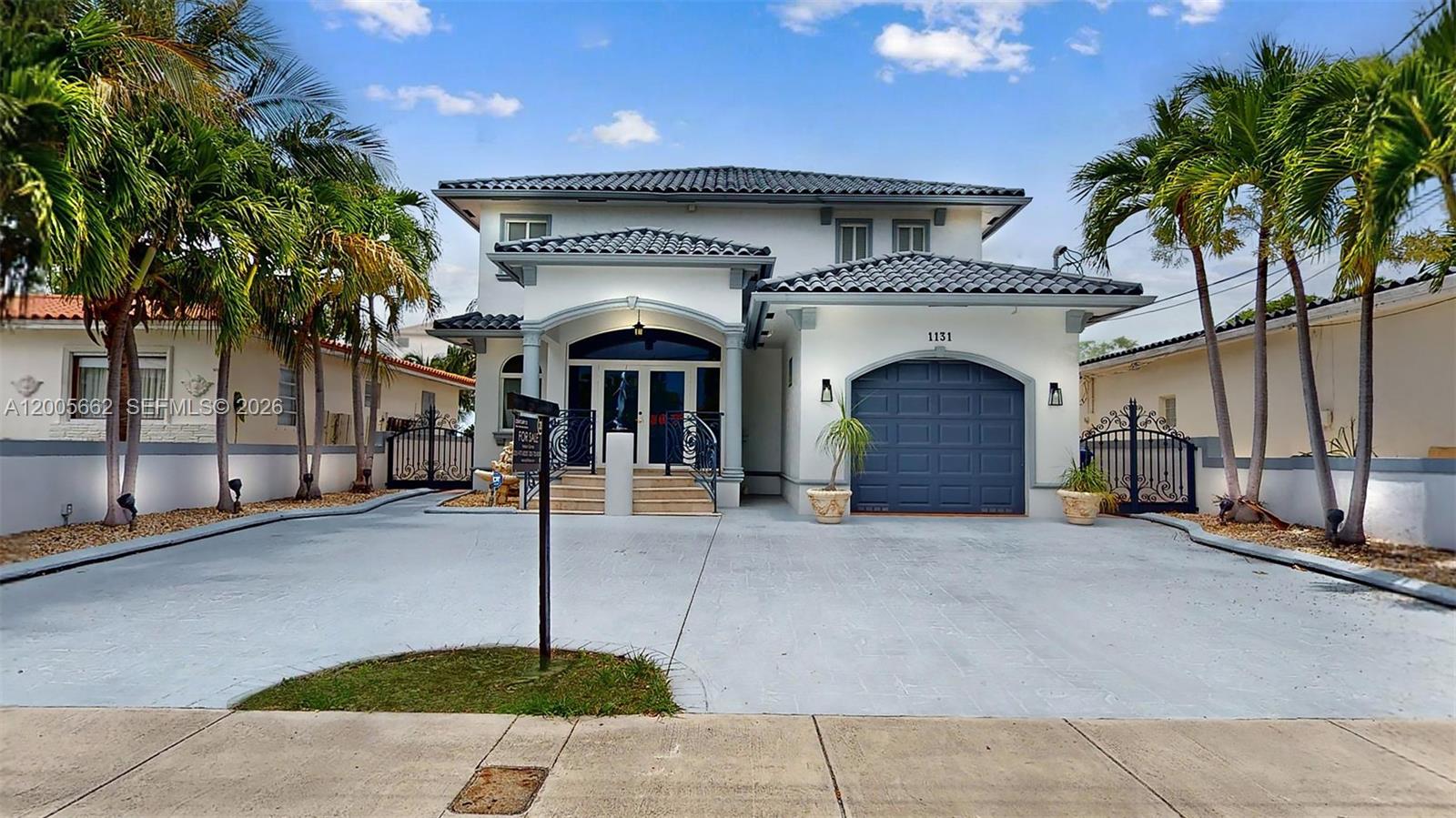 A two-story house with a gray tile roof, a blue garage door, and palm trees — 1131 Stillwater Dr, Miami Beach FL 33141, MIAMI BEACH, FL