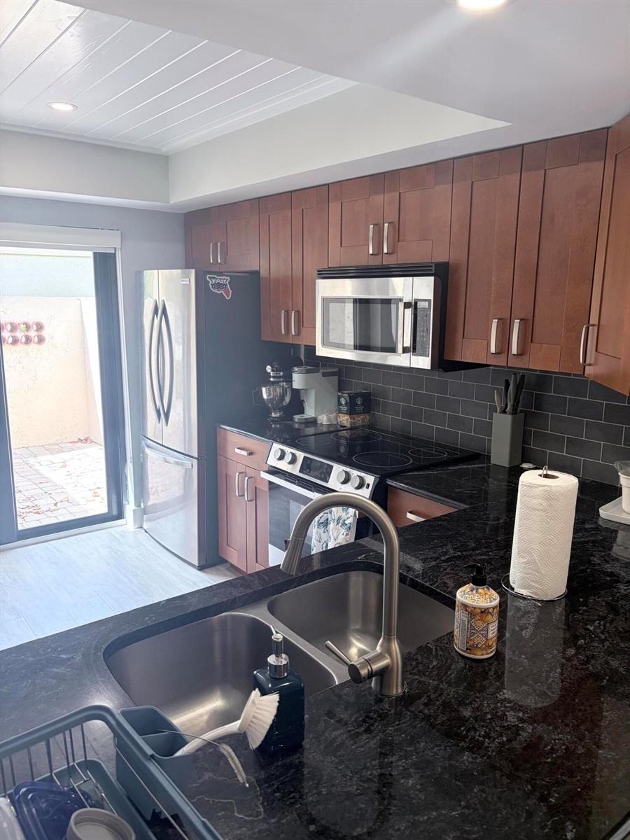 A kitchen features dark wood cabinets, black granite countertops, stainless steel appliances, and a subway tile backsplash — 3072 Inglewood Terrace, Boca Raton FL 33431, BOCA RATON, FL