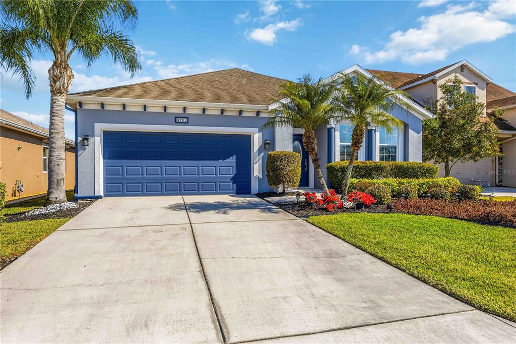 A single-story suburban house with a blue garage door, palm trees, and a landscaped yard — 5731 ARBOR WOOD COURT, BRADENTON, FL