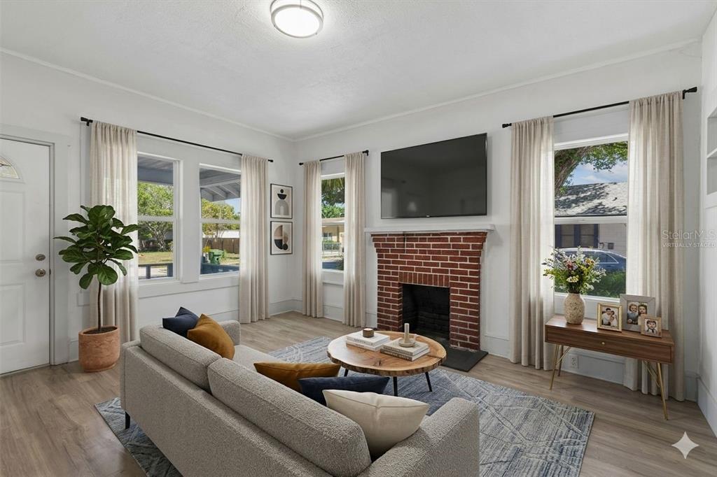 A living room features a brick fireplace, a mounted television, and light wood-look flooring — 1002 23RD STREET W, BRADENTON, FL
