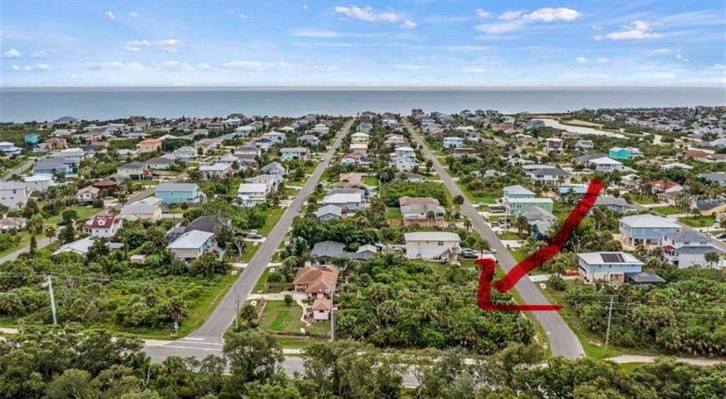 An aerial view shows a coastal neighborhood with a red arrow pointing to a vacant lot — 6235 N OCEAN SHORE BOULEVARD, PALM COAST, FL