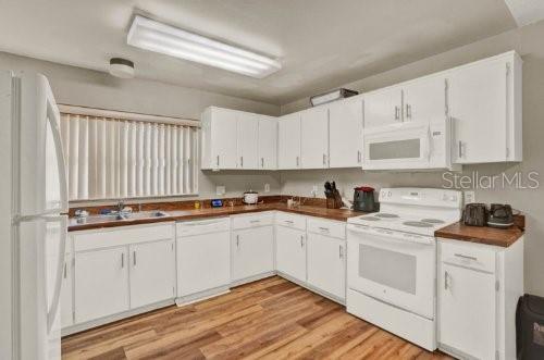 A kitchen features white cabinets, laminate countertops, wood-look flooring, and white appliances — 451 HUNTER CIRCLE, KISSIMMEE, FL