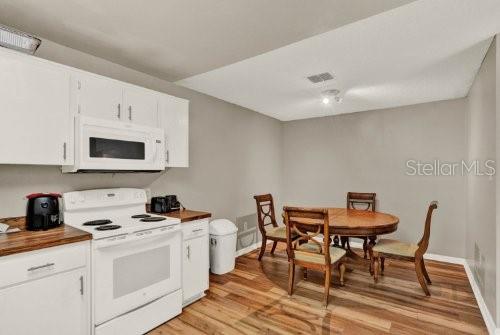 A kitchen with white cabinets, a white stove, and a wooden dining table with chairs — 451 HUNTER CIRCLE, KISSIMMEE, FL