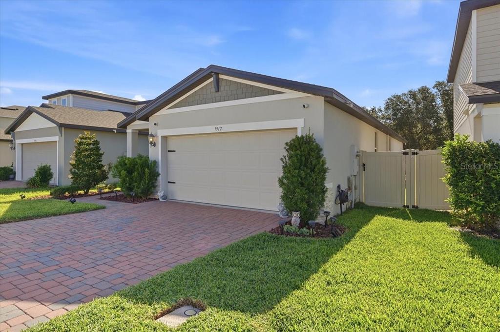 A single-story house with a beige stucco exterior, a brick driveway, and a garage — 1912 CARNOSTIE ROAD, WINTER HAVEN, FL
