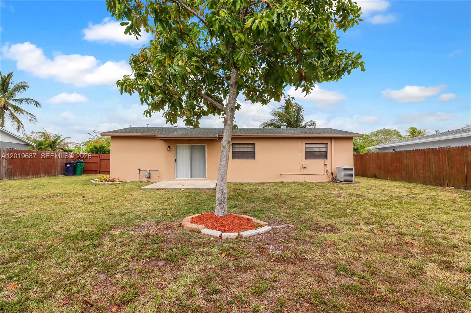 The exterior of a single-story house features a tan stucco wall, sliding glass doors, and a tree — 15502 SW 102nd Ave, Miami FL 33157, MIAMI, FL