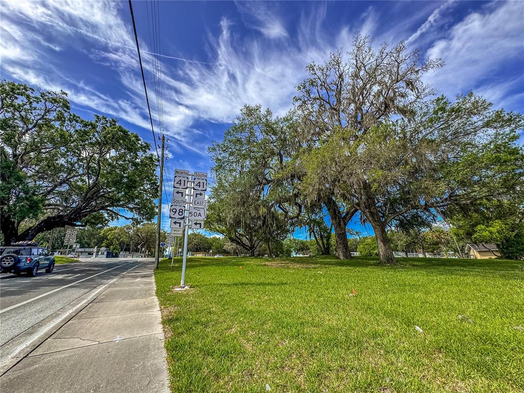 A grassy lot with large oak trees sits next to a sidewalk and road intersection — 615 OLD HOSPITAL DRIVE, BROOKSVILLE, FL