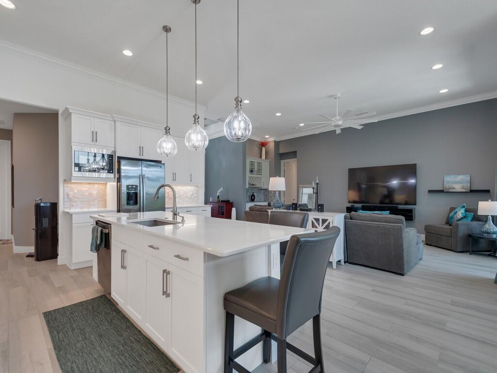 A modern open-concept kitchen with a white island and pendant lights overlooks a living area — 8220 Halbert Lane, Vero Beach FL 32968, VERO BEACH, FL