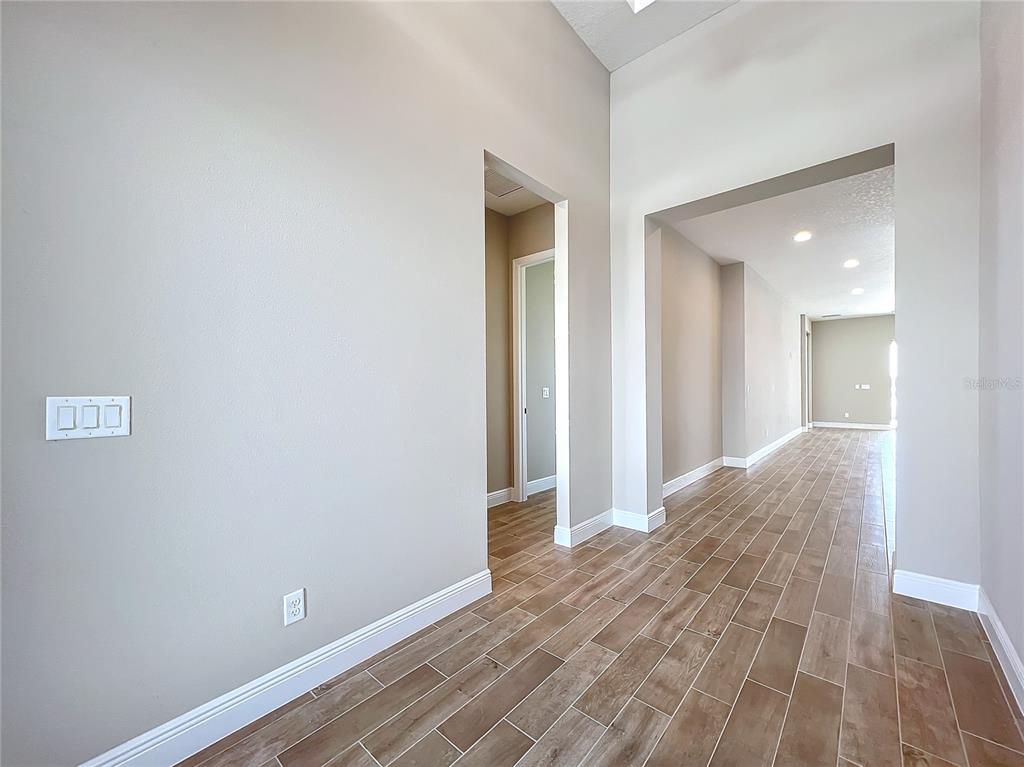 A hallway with light-colored walls and wood-look tile flooring leads toward an open living area — 247 MONET TRAIL, BRADENTON, FL