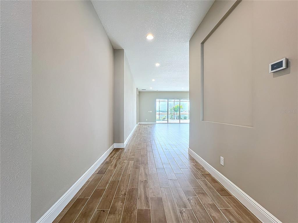 A hallway with wood-look tile flooring leads toward a living area with sliding glass doors — 247 MONET TRAIL, BRADENTON, FL